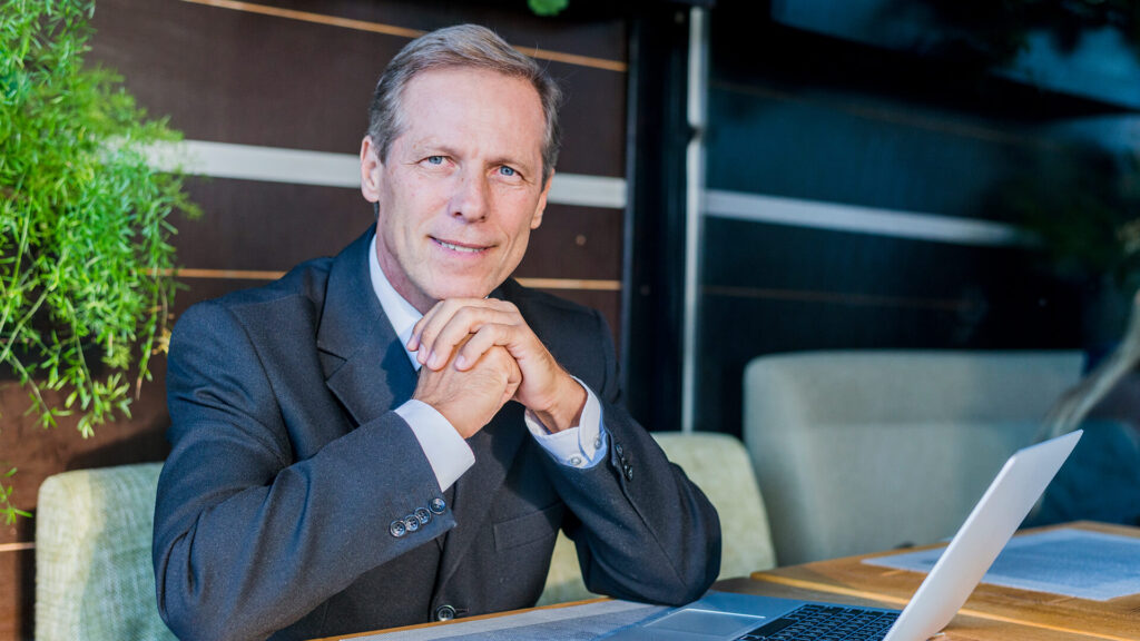 Portrait of a mature businessman founder with laptop over desk in restaurant